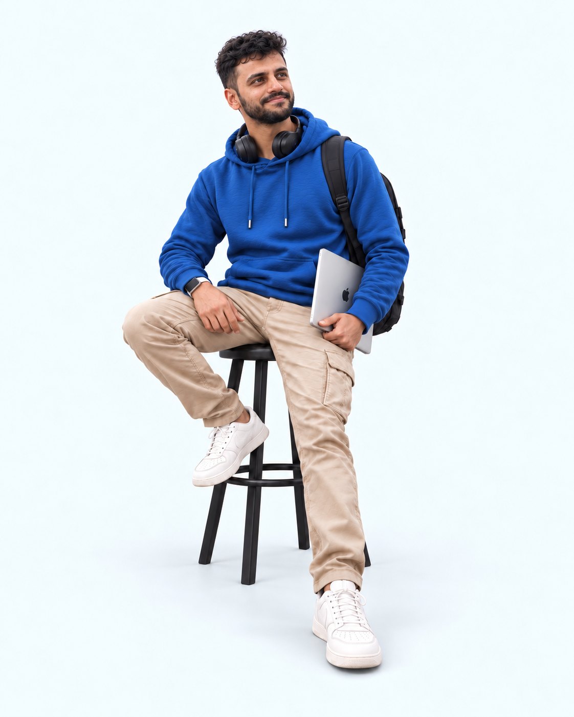 Harish sitting on a stool in a blue hoodie, holding a laptop